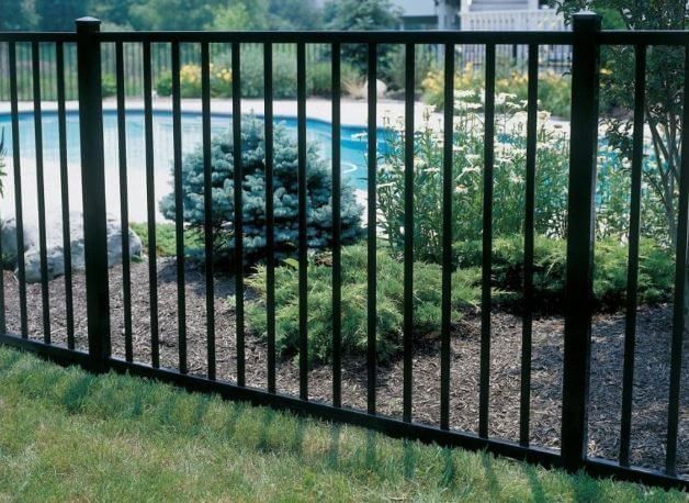 Black metal fence in front of a backyard pool and landscaped garden.