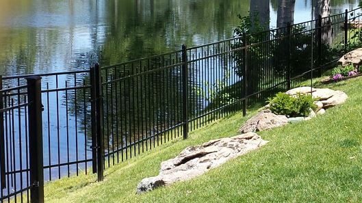 Black metal fence along a pond beside a grassy slope and landscaped rocks