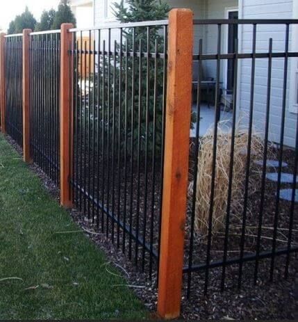 Black metal fence with wood posts along a grassy yard beside a house