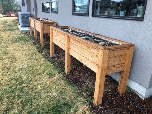 Three wooden raised garden beds beside a house wall on a grassy lawn