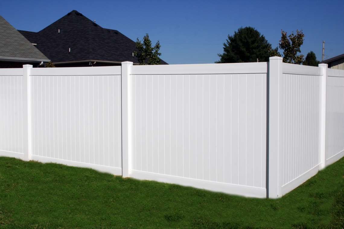 White vinyl privacy fence surrounding a green lawn under a clear blue sky