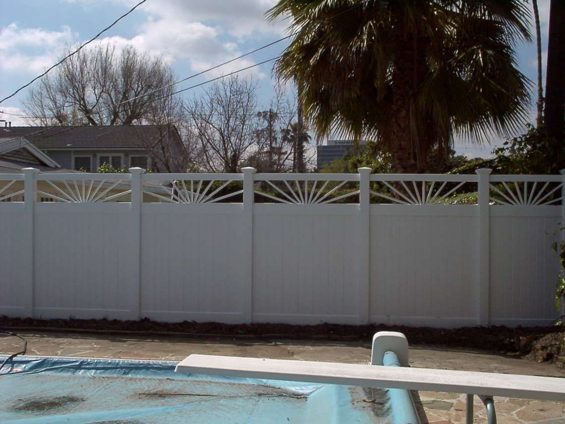 Backyard with a white fence and swimming pool under a partly cloudy sky