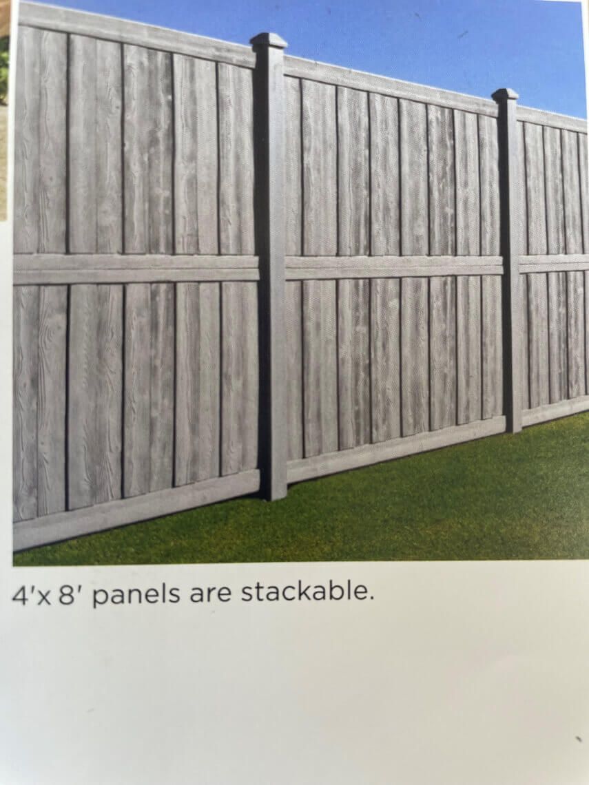 Stacked gray 4x8 fence panels with posts on a grassy lawn under a blue sky.