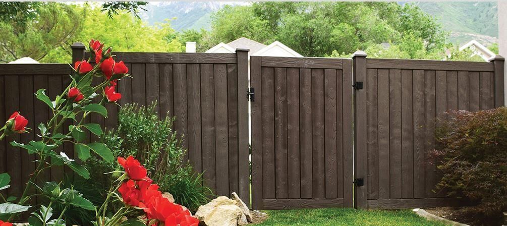 Wooden backyard fence with red flowers in the foreground and green trees beyond