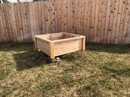 Wooden raised garden bed in a grassy backyard with a tall wooden fence.