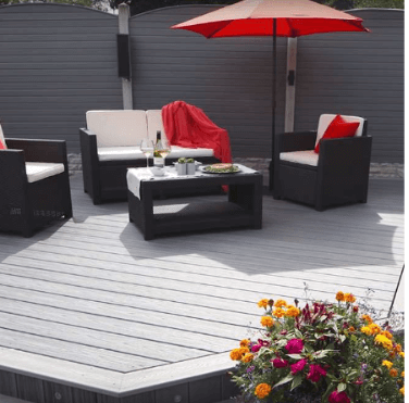 Patio deck with black lounge chairs, red umbrella, coffee table, and flowers in the foreground