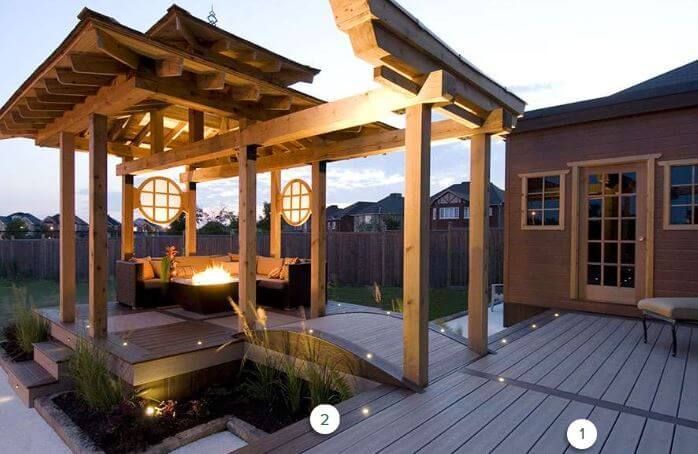 Wooden patio deck with a lit pergola seating area and modern house exterior at dusk