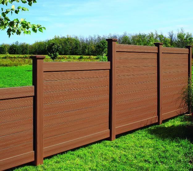 Brown wooden privacy fence along a green lawn under a bright blue sky