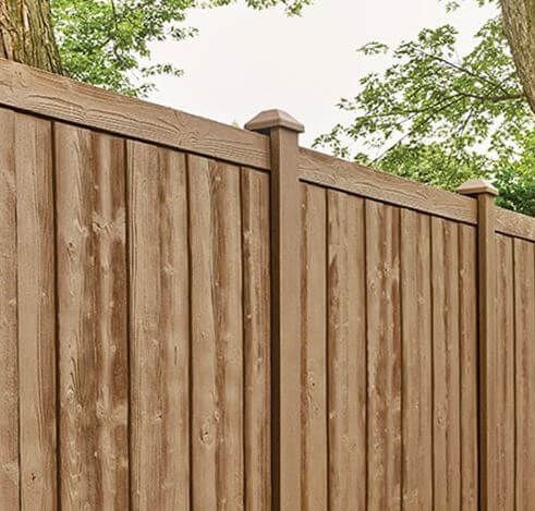 Wooden privacy fence with vertical slats and capped posts beneath leafy green trees