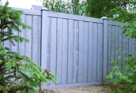 Gray wooden fence with a gate, surrounded by green trees and shrubs.