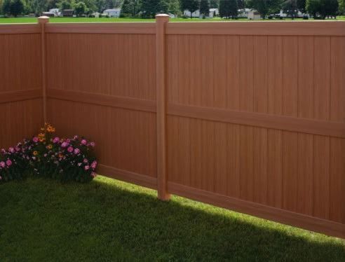 Brown wooden fence beside a green lawn with a small pink flower bed in the corner