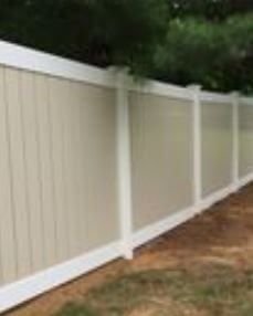 Beige vinyl privacy fence along a yard with trees and dirt edge