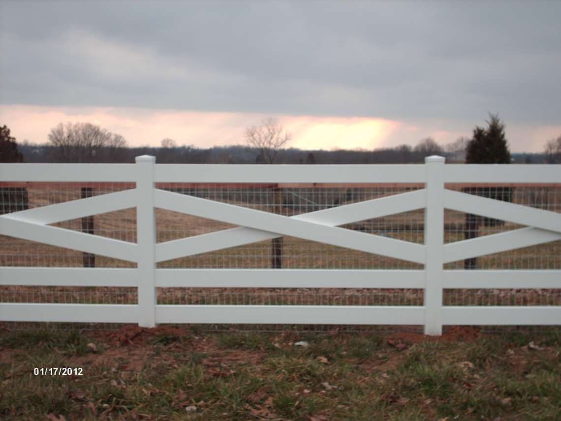 White wooden fence with diamond crossbars in a rural field under a cloudy sky.