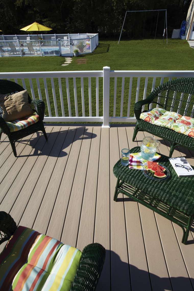 Deck with wicker chairs and colorful cushions overlooking a grassy yard and fence
