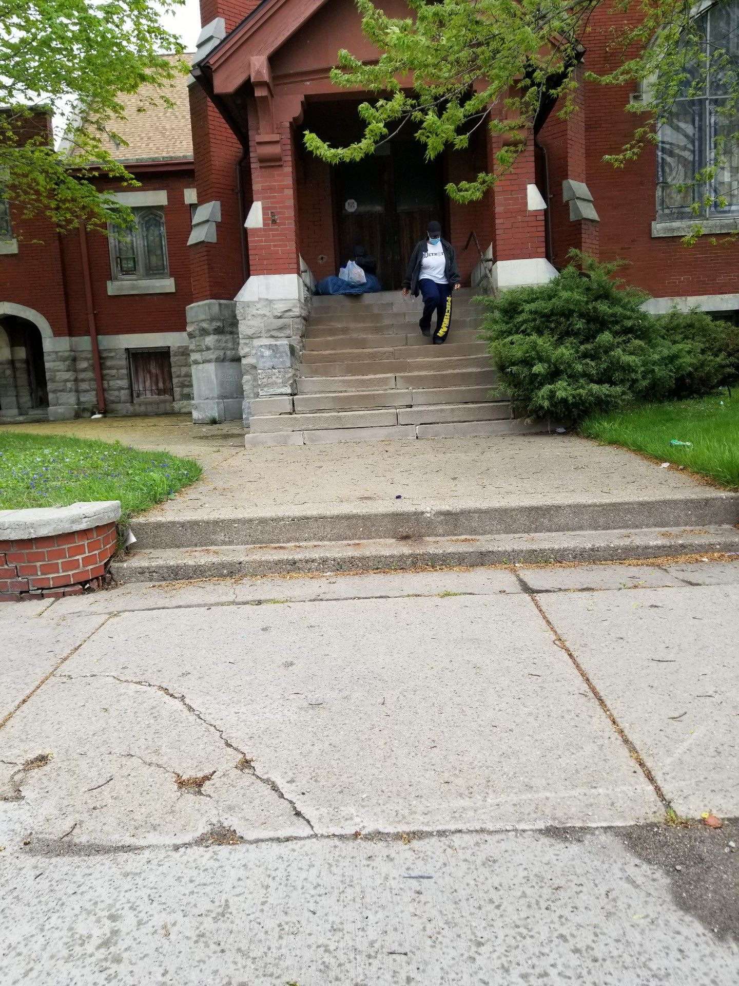 Brick building entrance with stone steps, two people near the doorway, and a sidewalk in front
