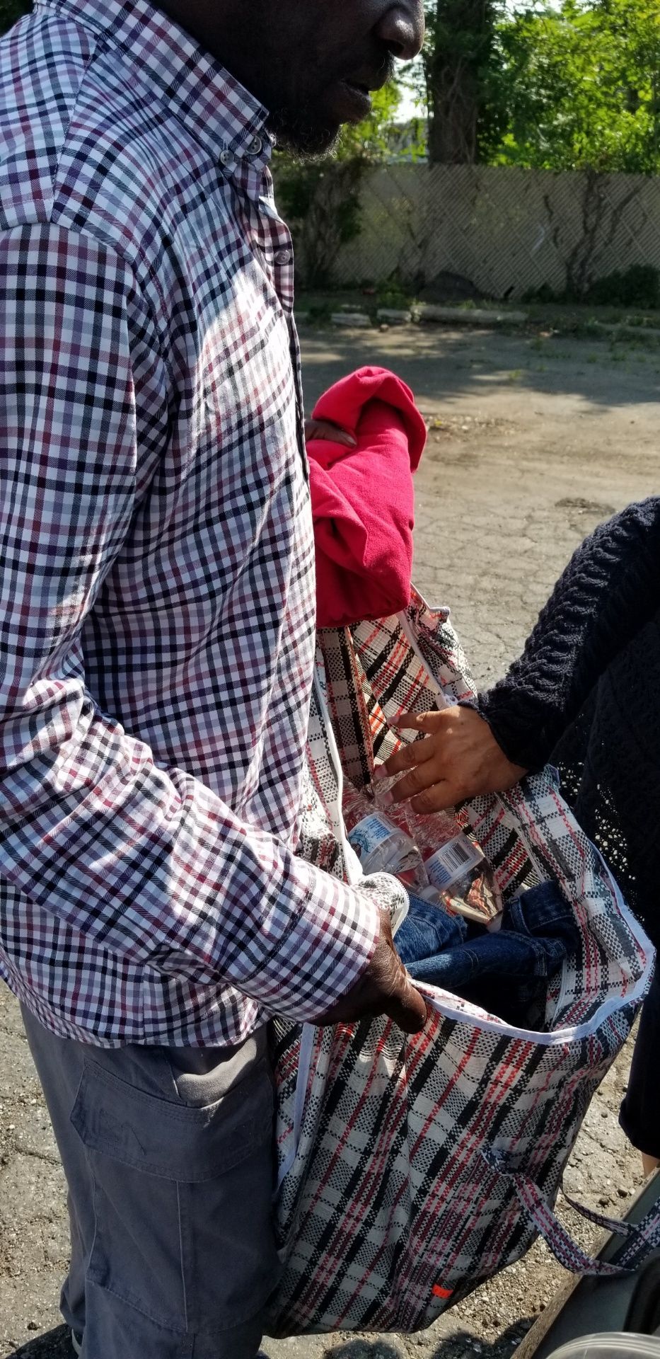 Person holding open a large plaid bag beside another person in a red jacket outdoors