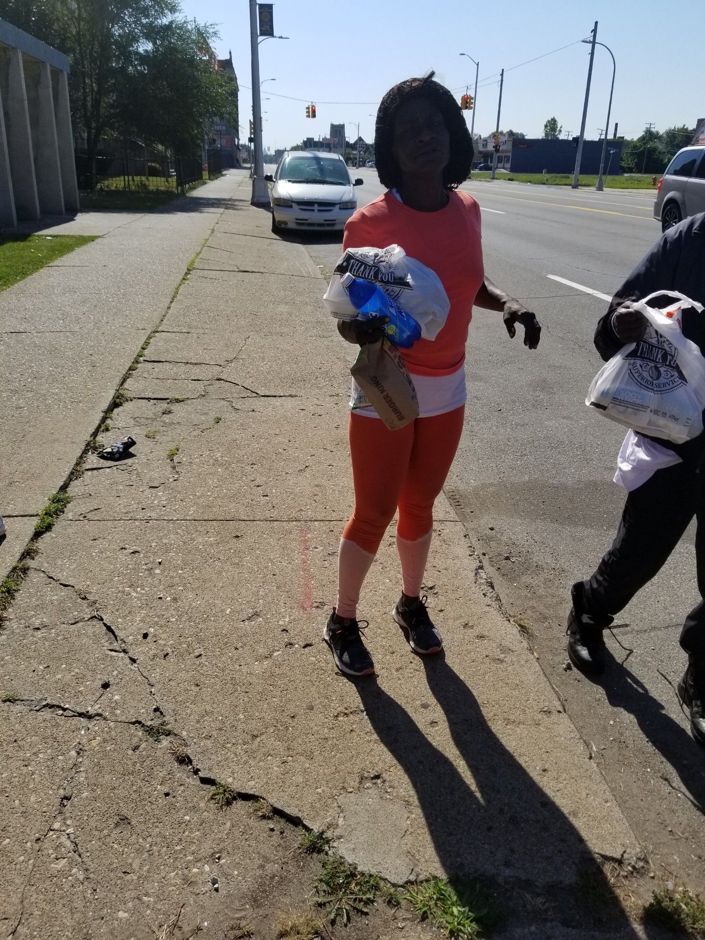 Person standing on a sidewalk holding flowers, with another person partially visible beside them.