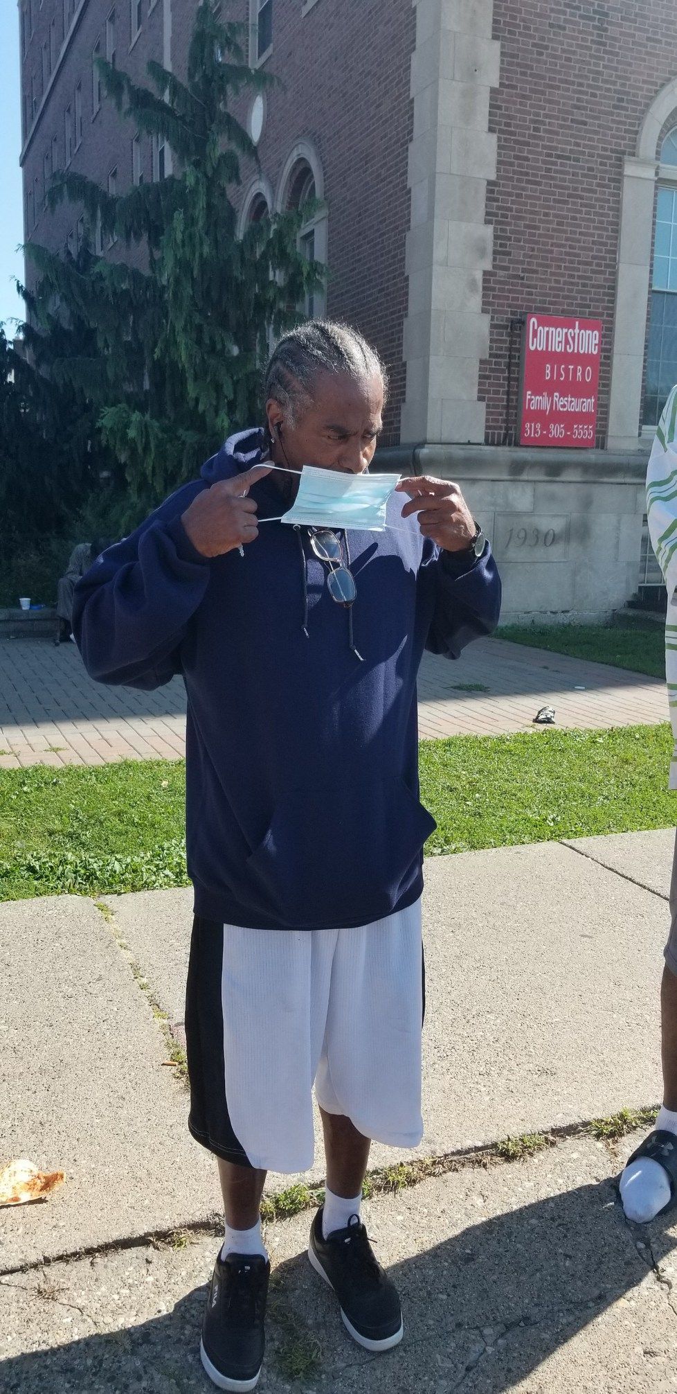 Person standing outdoors on a sidewalk holding up a clear cup in front of a building.