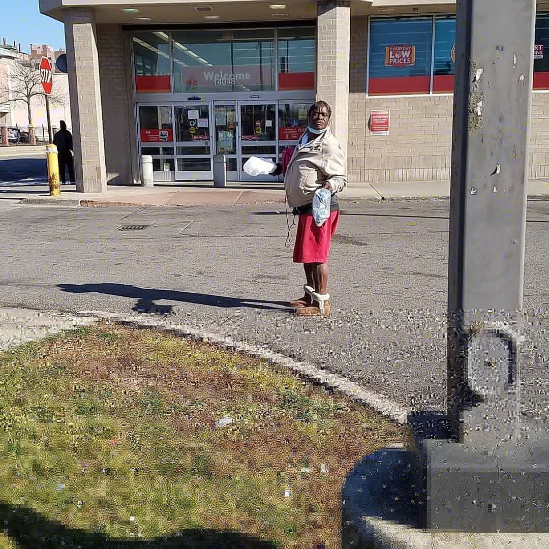 Person standing outside a storefront on a sunny day, near a sidewalk and parking lot.