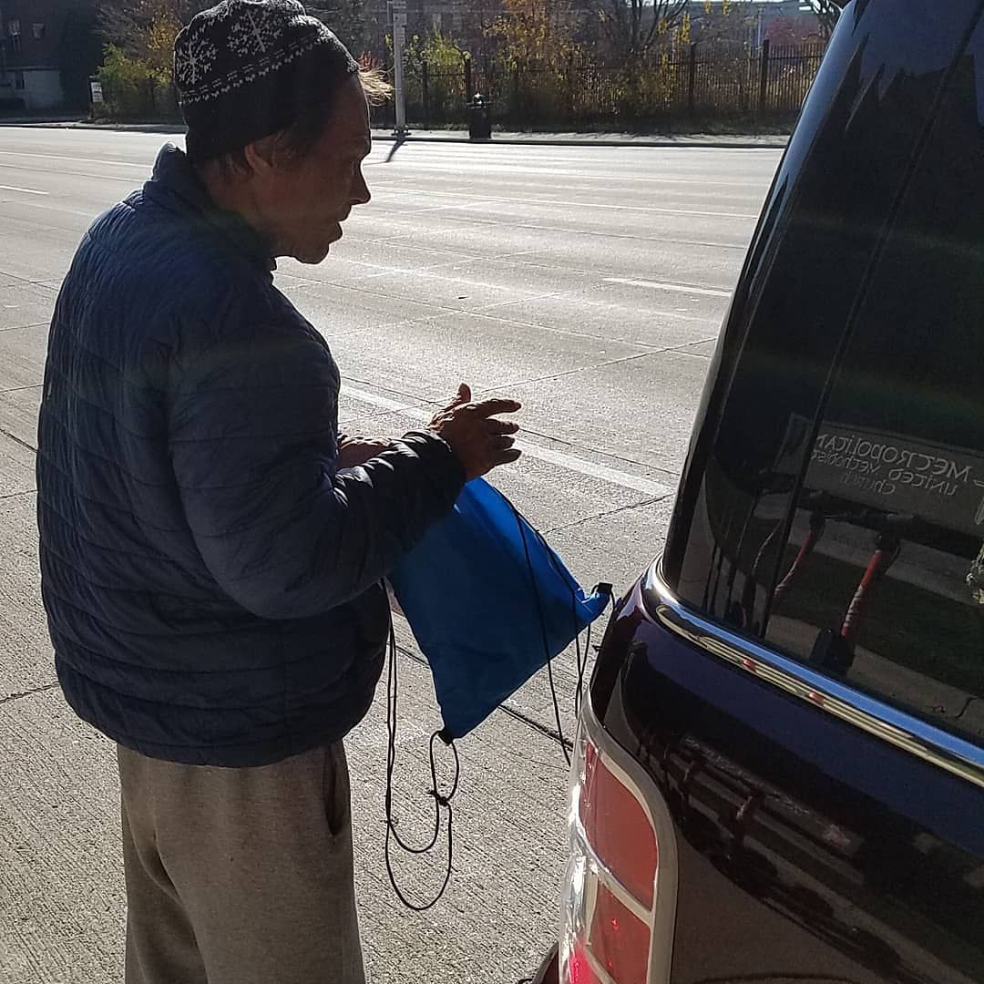 Person beside a black vehicle holding a blue bag on a sunny street