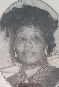 Black-and-white portrait of a person with curly hair, wearing a patterned shirt and hoop earrings.