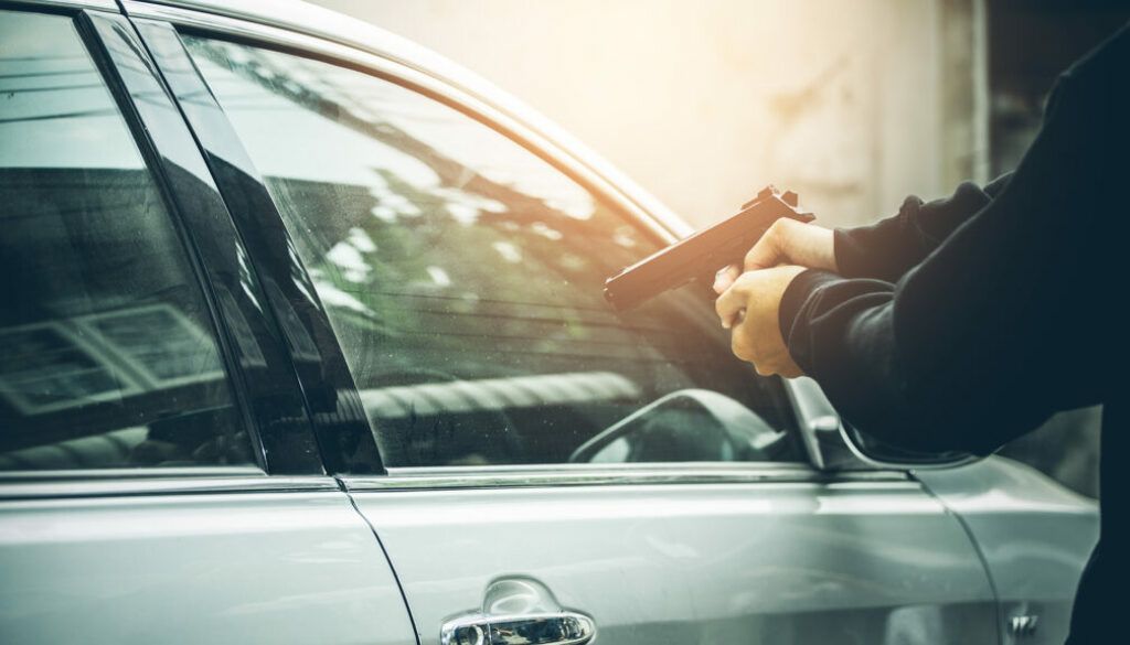 A person pointing a gun at the window of a vehicles