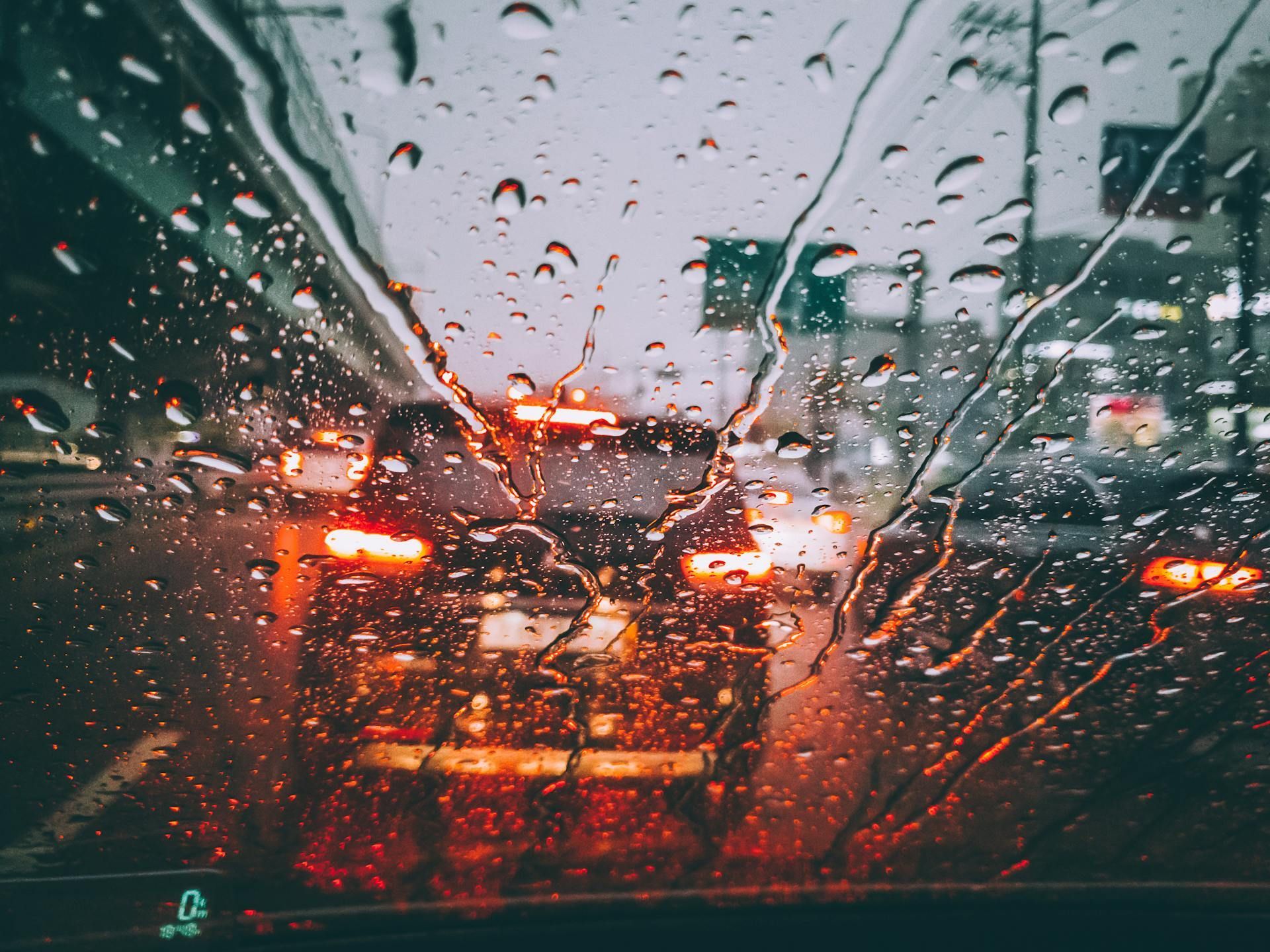 The interior of a car windscreen, rain runs down it while the car is in traffic
