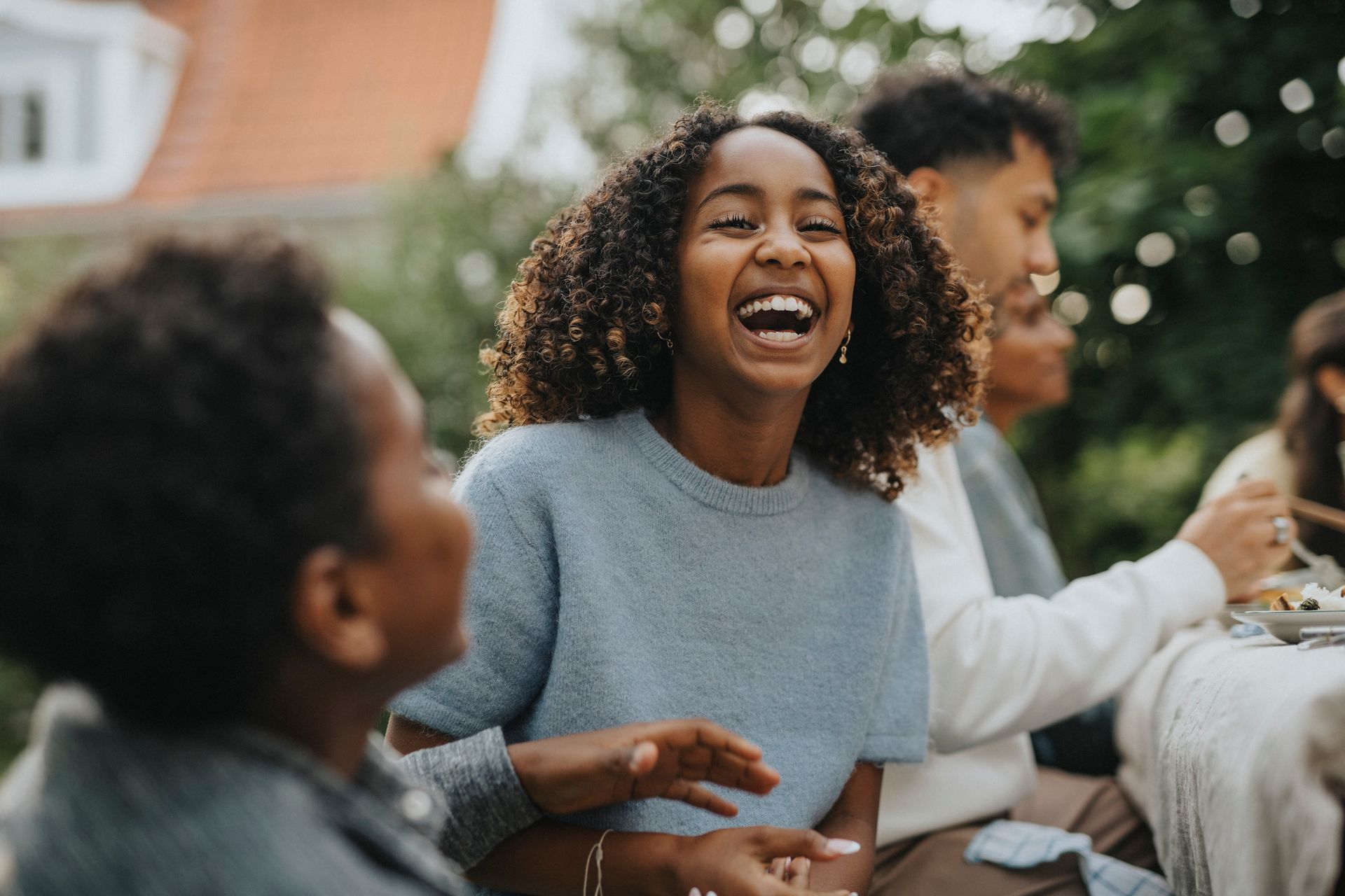 Woman with curly hair laughs at an outdoor gathering with family.