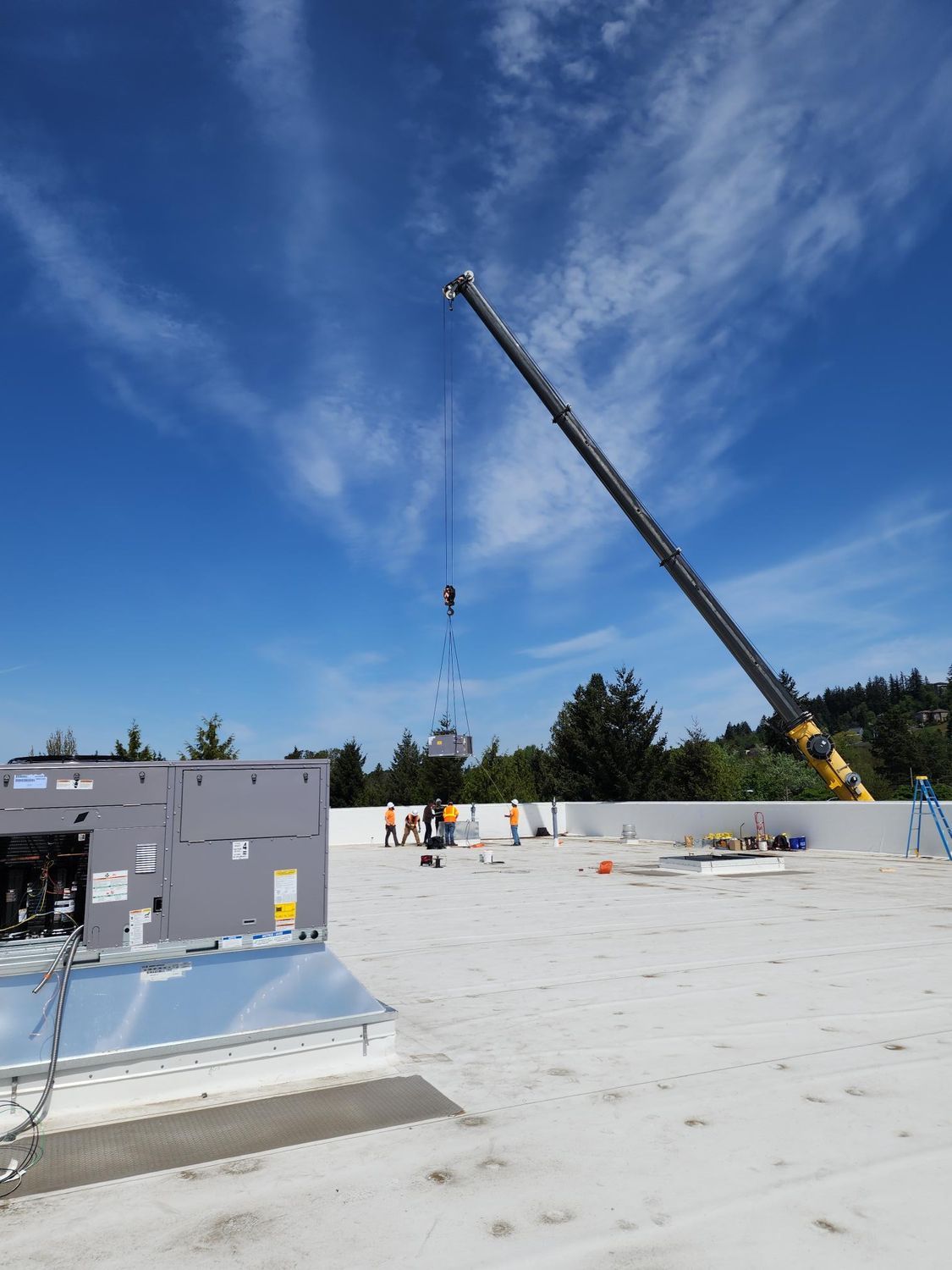 A crane is lifting a gray box on top of a white roof.
