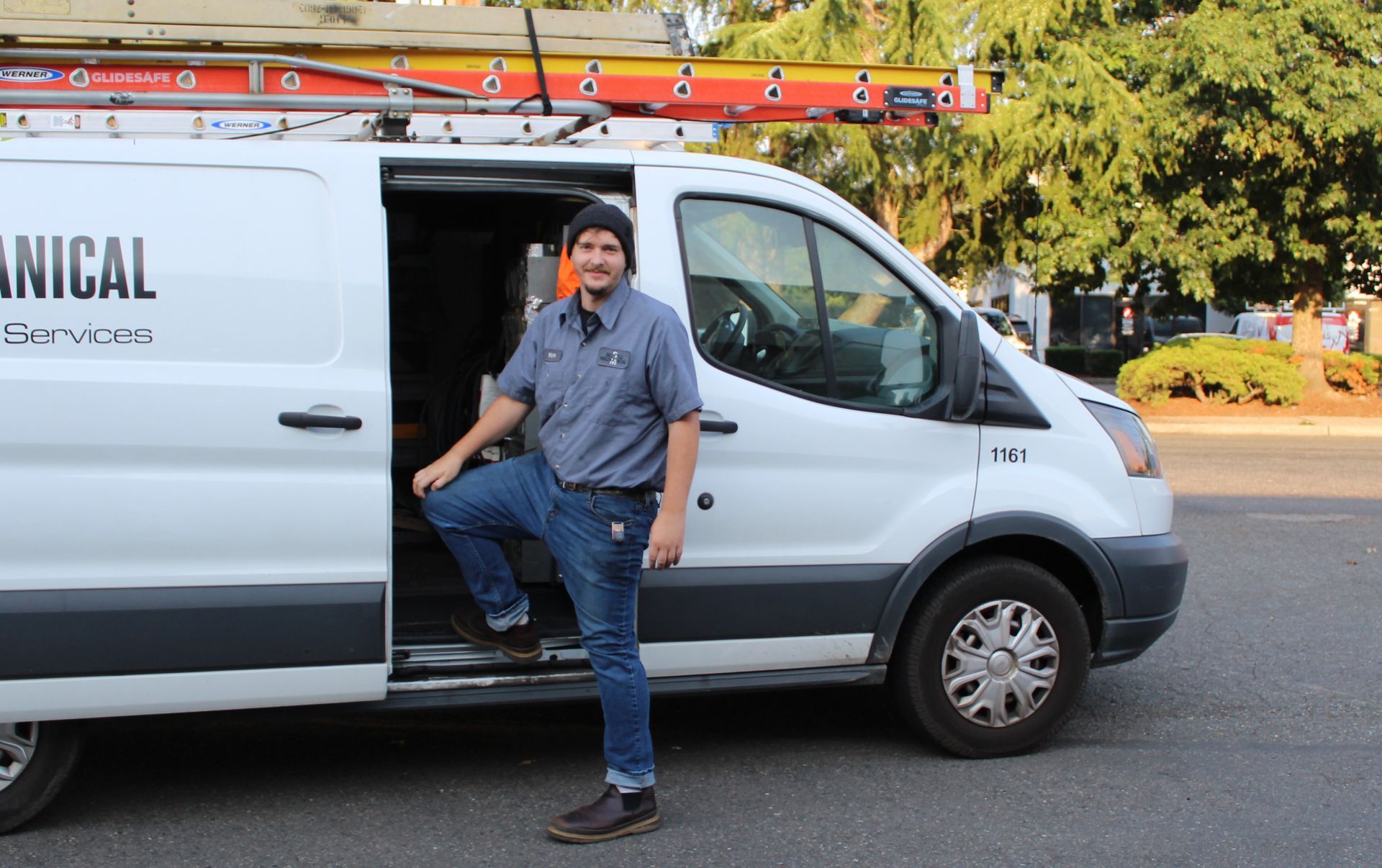A man is standing next to a white van that says mechanical on it
