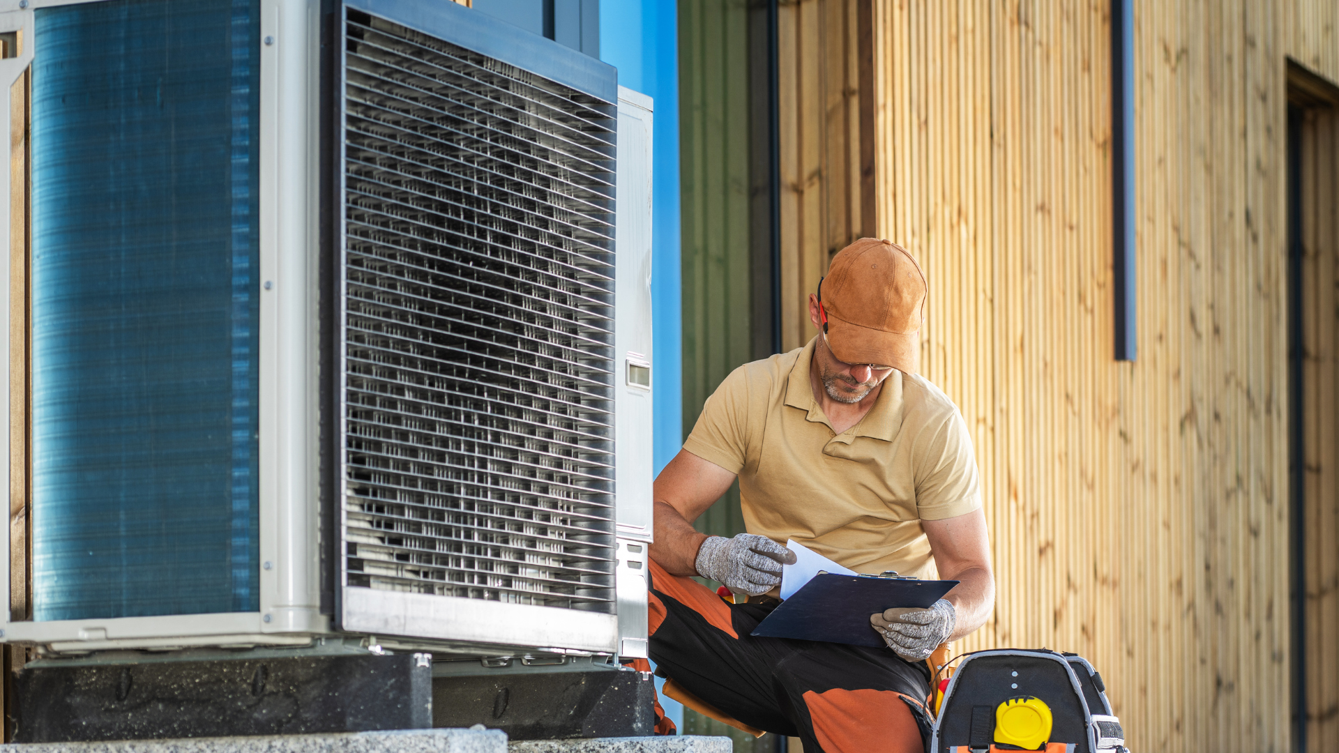 A man is sitting on a bench working on an air conditioner.