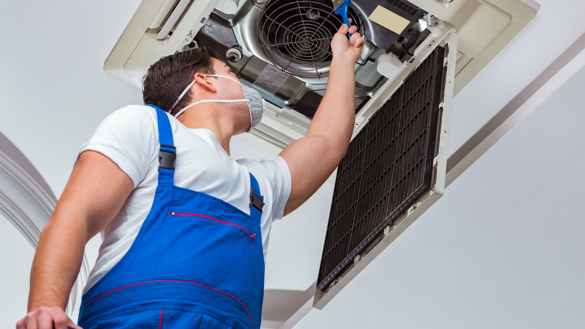 A man wearing a mask is working on an air conditioner.