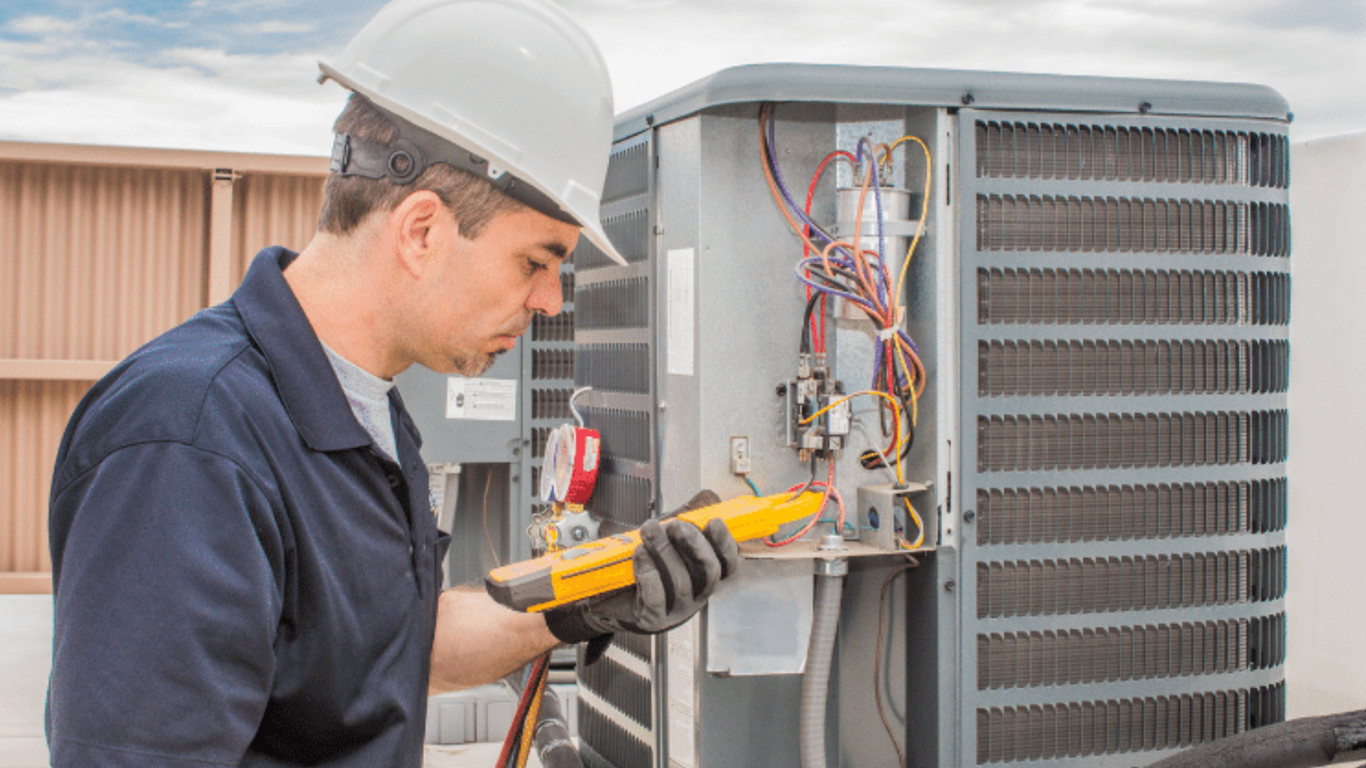 A man wearing a hard hat is working on an air conditioner.
