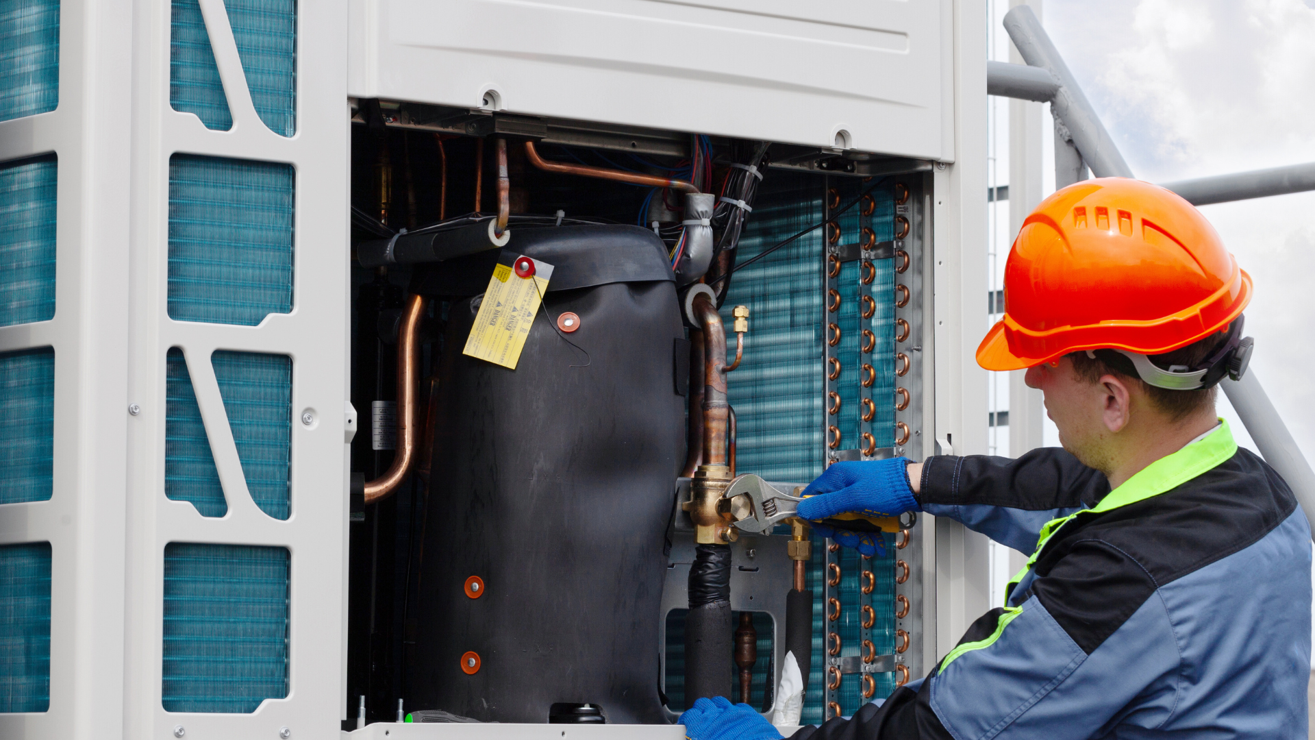 A man wearing a hard hat is working on an air conditioner.