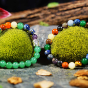 Two green moss balls with colorful beaded rings on a rustic surface