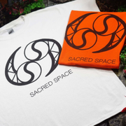 White and orange Sacred Space T-shirts with a black circular logo laid out side by side