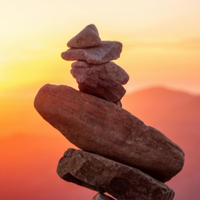 Stacked stones silhouetted against a warm orange sunset sky