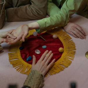 Hands around a red tabletop board game with colorful stones and a yellow fringe
