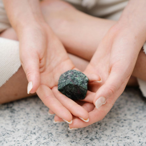 Hands holding a dark green stone over a speckled countertop