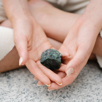 Hands holding a dark green stone over a speckled countertop