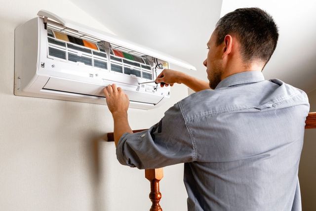 Technician cleaning a wall-mounted air conditioner with the cover open
