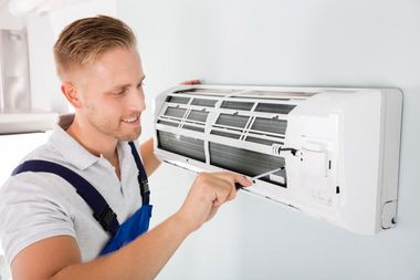 Technician servicing a wall-mounted air conditioner with the front panel open