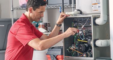 Technician in red shirt working on an open HVAC unit with tools in a utility room