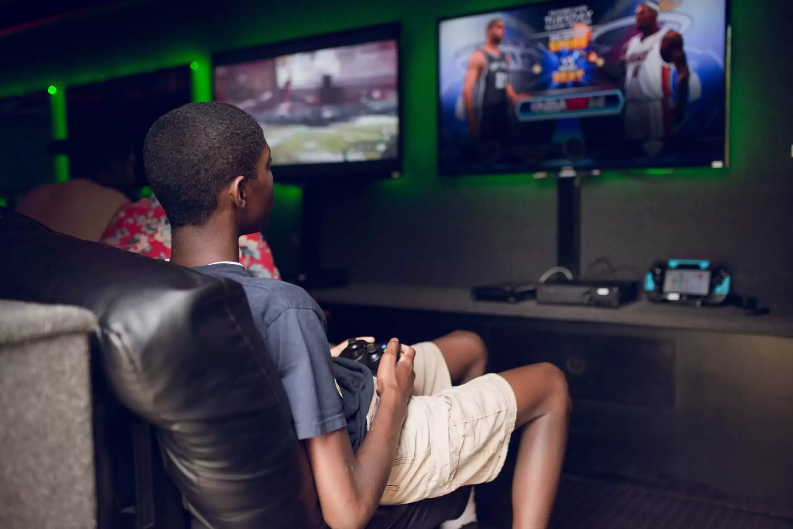 A young Black person sits playing a video game in a gaming lounge, focused on the screen.