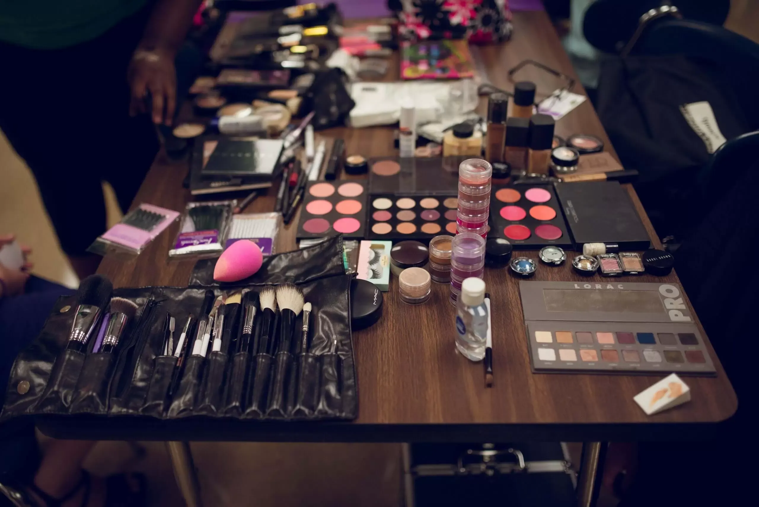Makeup artist's table: Makeup brushes, palettes, compacts, and beauty blenders on a table in a room.
