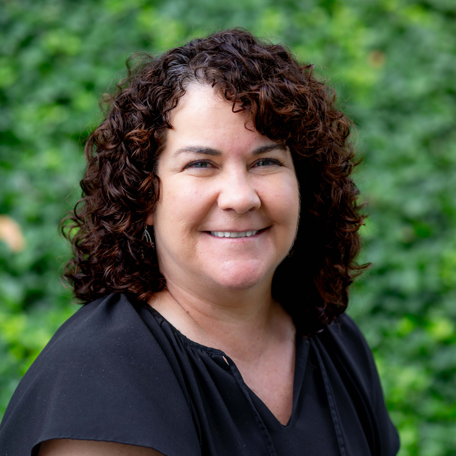 Woman with curly brown hair wearing a red sweater and black shirt, smiling.