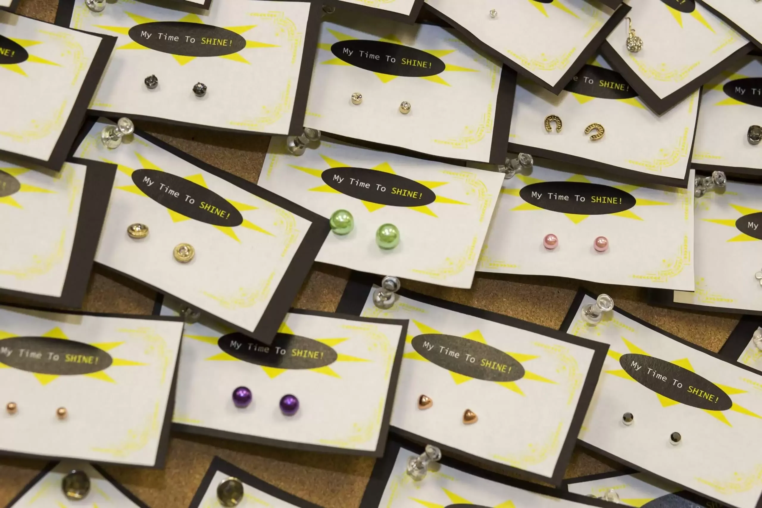 Earrings displayed on cards pinned to a corkboard. Various colors and styles visible.