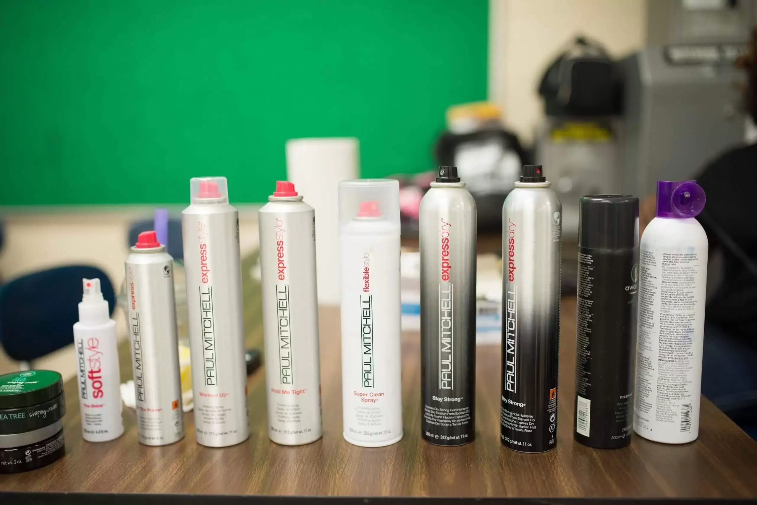 Various hairspray bottles on a table with a green background.