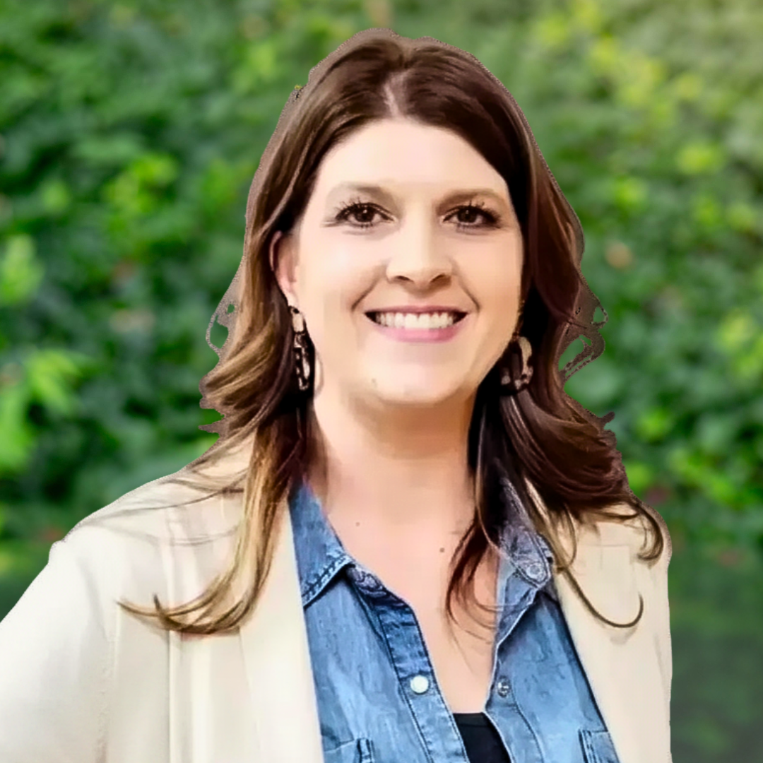 Woman with brown hair smiles, wearing a blue denim shirt and beige jacket.