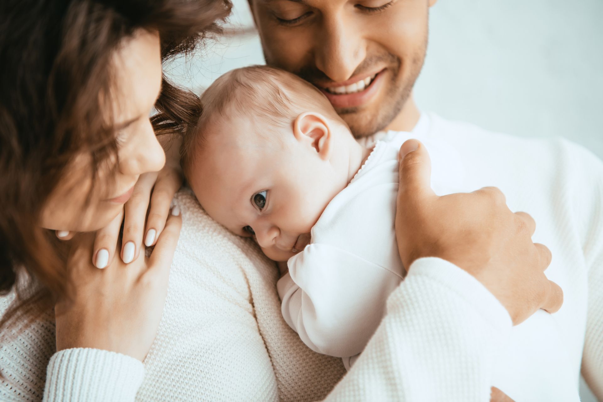 Parents smiling, holding baby wrapped in white.